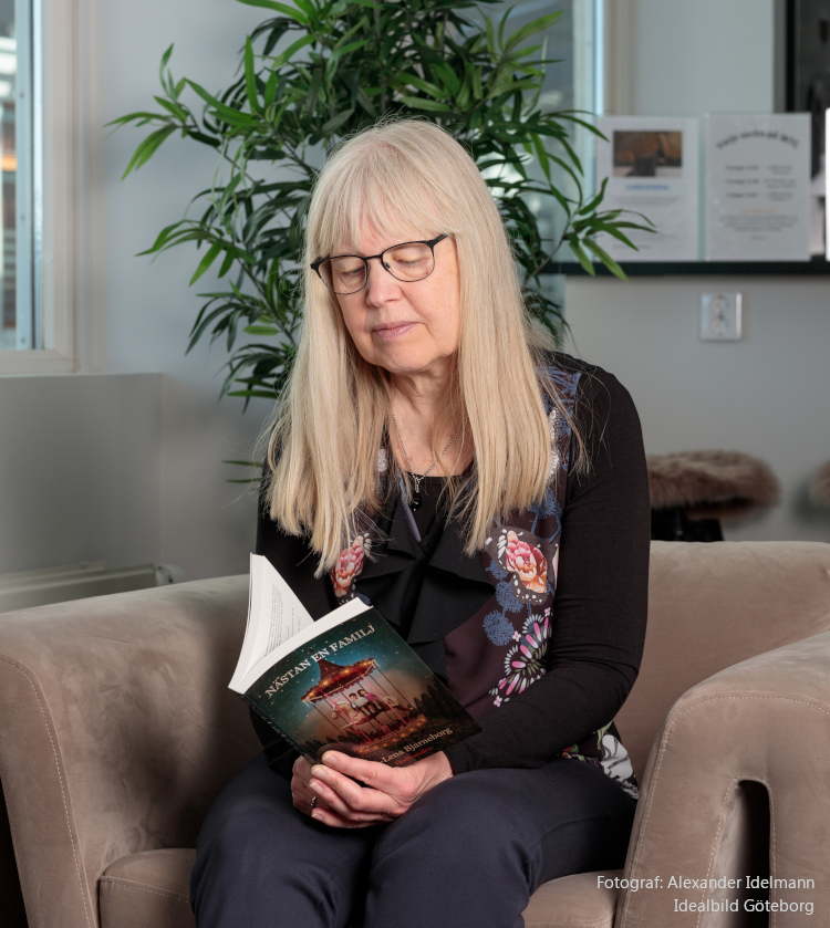 Eva-Lena sitter i en fåtölj och tittar i sin bok Nästan en familj.